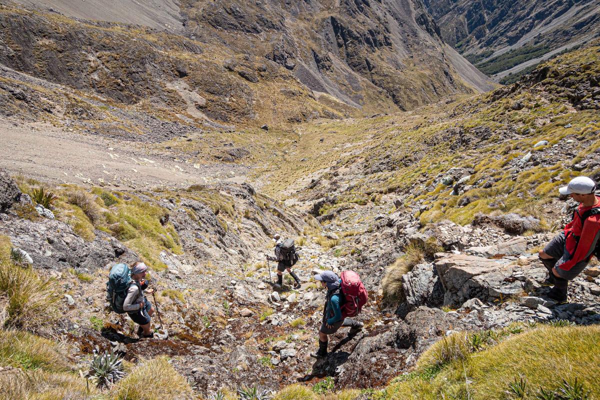 Four trampers cross a steep, dry creek bed