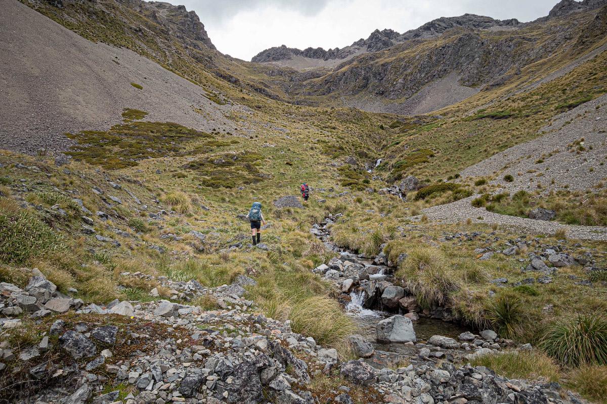 Two trampers walk up a valley next to a stream