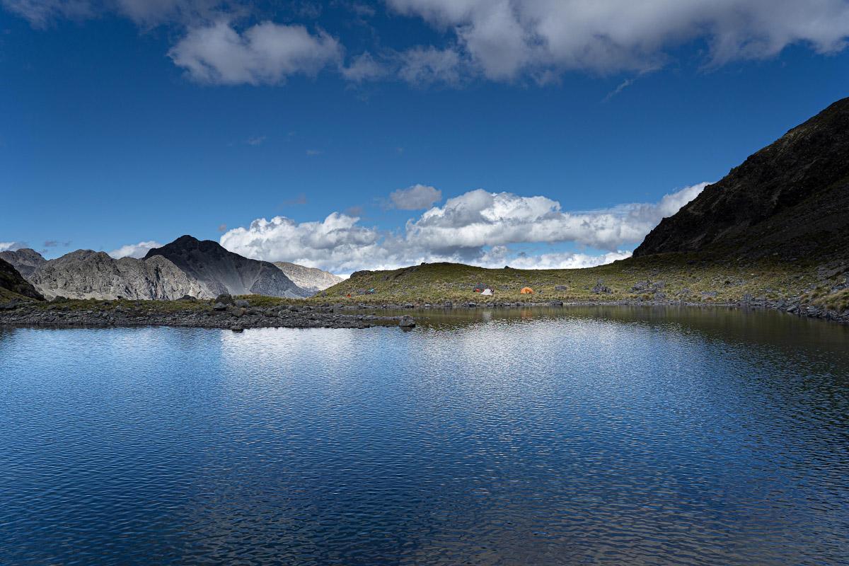 View across a tarn to two tents with mountains in the background