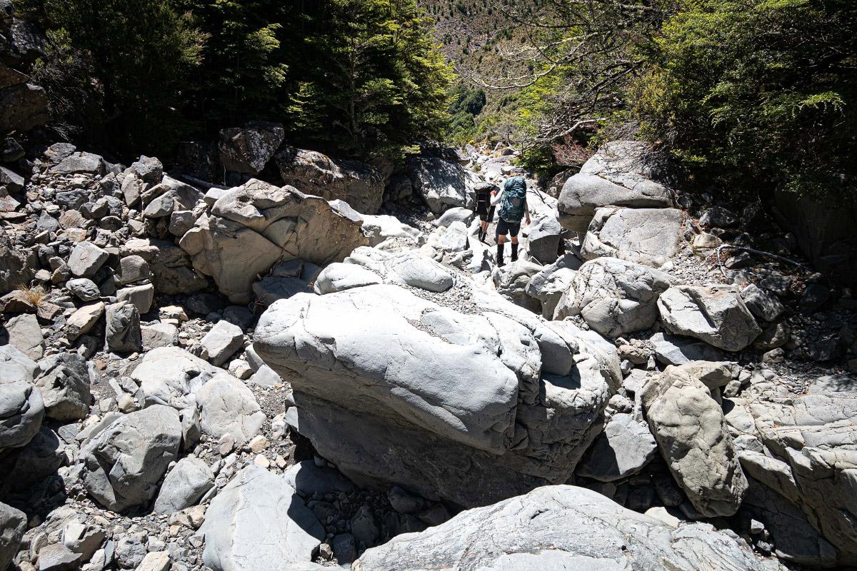 Two trampers follow a boulder-strewn dry creek bed