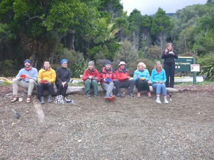 Group of nine people eating food on a log