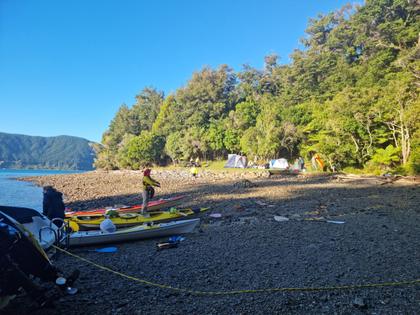 People getting up as the sun rises on a beach with beached kayaks and tents in the background