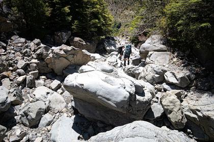 Two trampers follow a boulder-strewn dry creek bed