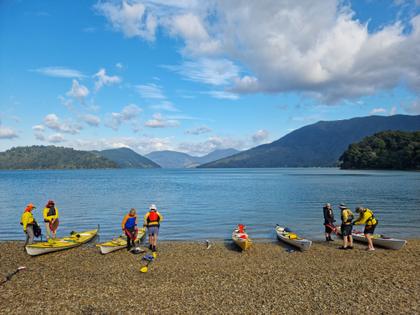 Seven people and five kayaks prepare to take to the water from the beach