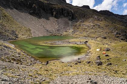 A green alpine tarn with two tents set up nearby