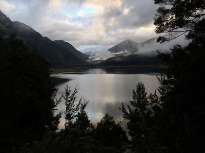 View over a lake with mountains and clouds. Trees in foreground