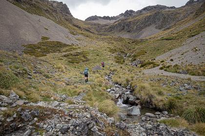 Two trampers walk up a valley next to a stream