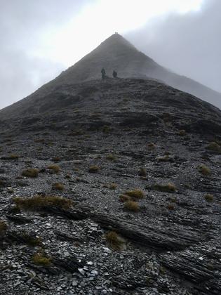 Two trampers descend from a peak in cloud. Two more remain on the summit
