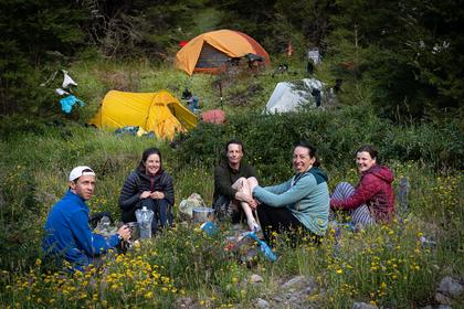 Five trampers at a campsite, three tents in background